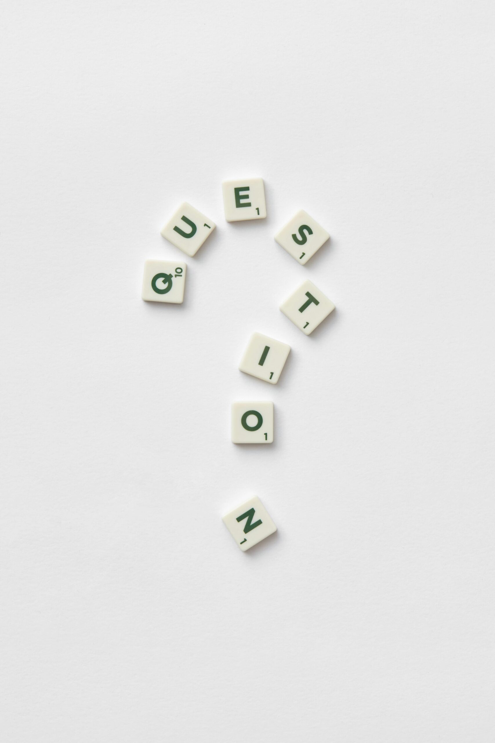 Artistic arrangement of letter tiles forming a question mark on a white background.