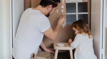 pexels-photo-3933227-3933227 Father and daughter painting a cardboard house indoors, enjoying quality time together.